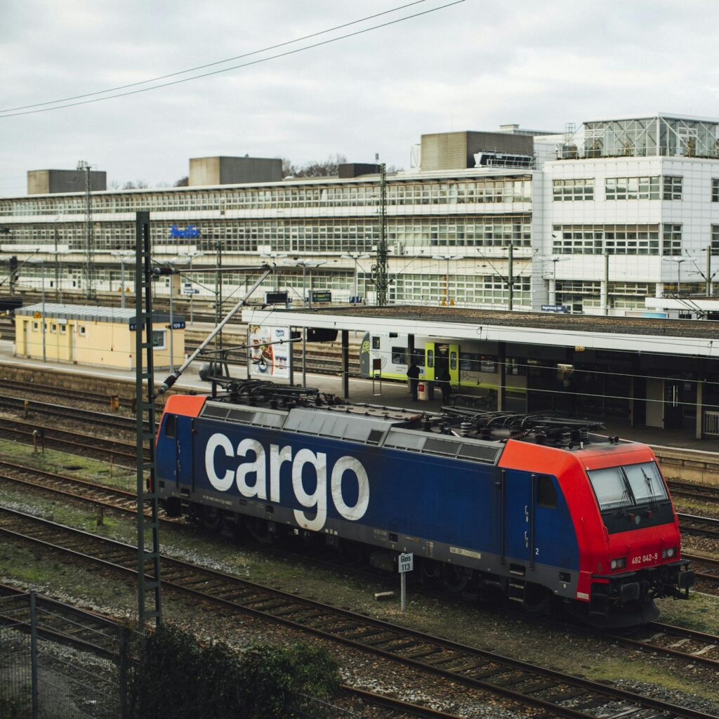 Cargo train parked at a modern urban railway station on a cloudy day.