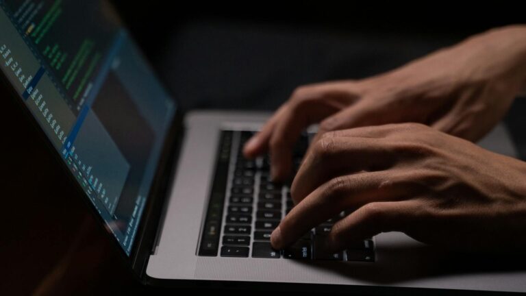 Hands typing code on a laptop keyboard in a dark room, capturing the essence of late-night programming.